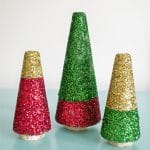 Three glitter styrofoam christmas trees in red, gold and green on a light blue table.