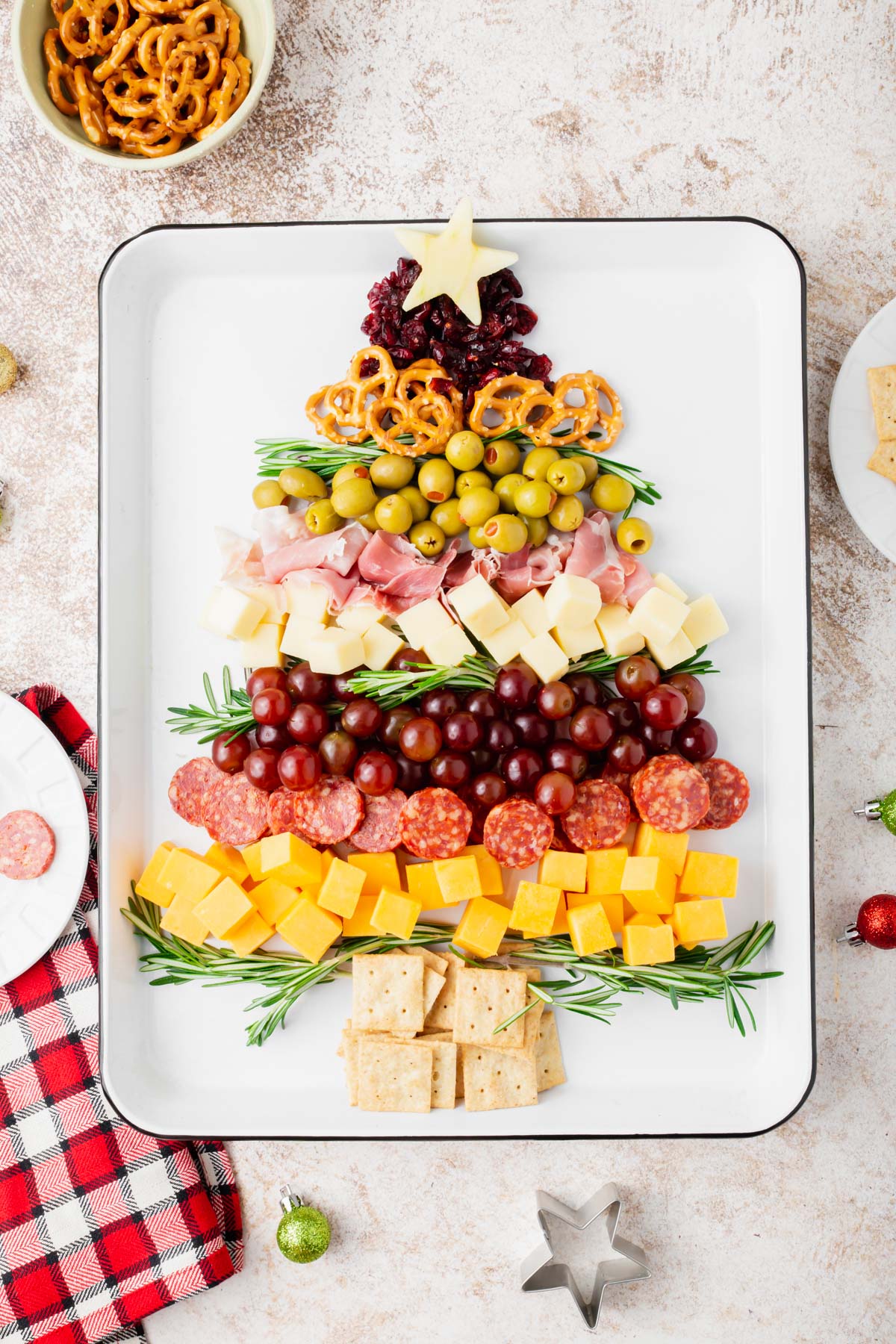 A charcuterie board in the shape of a Christmas tree with a star on top of a white tray.