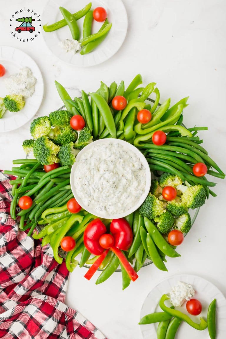 Green and red vegetables arranged in the shape of a wreath with a dip in the middle.