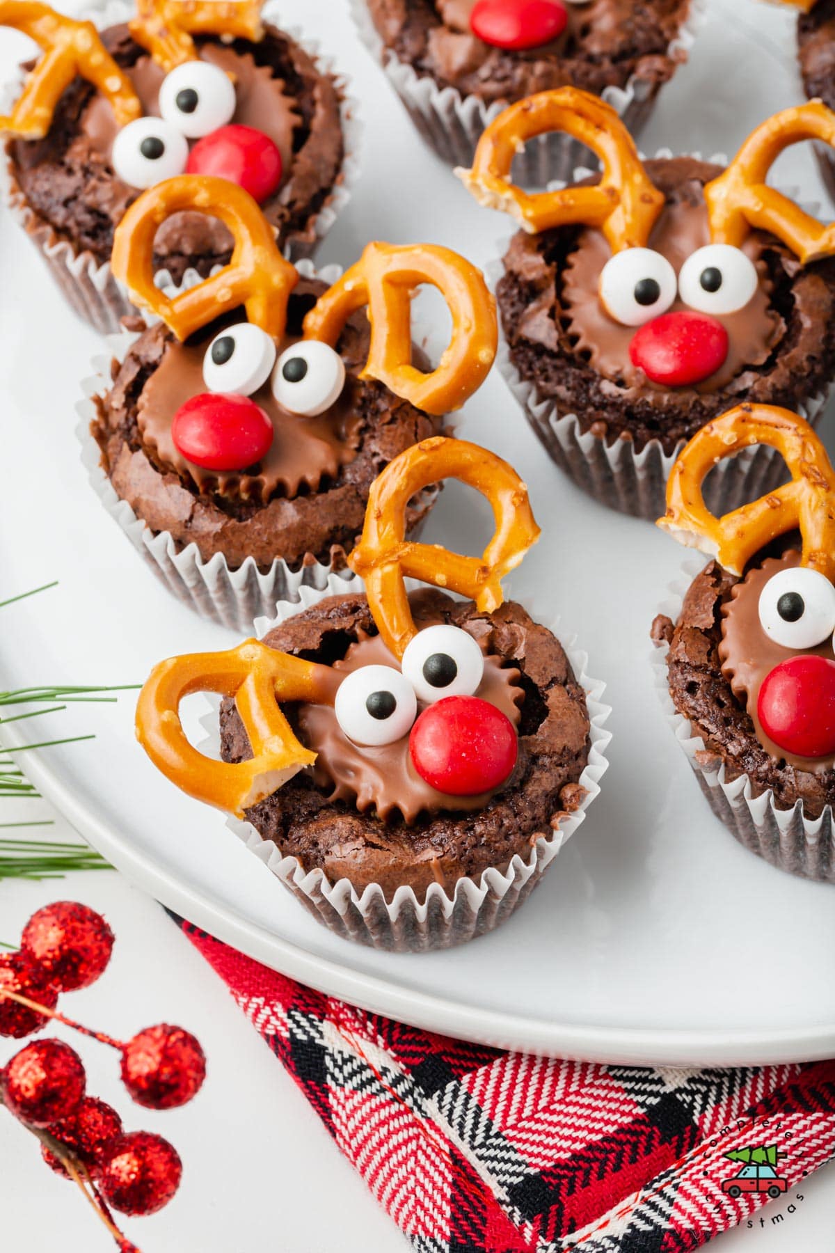 A tray of brownie cookie cups with a peanut butter cup made to look like a reindeer with pretzels for antlers and candies for the nose and eyes.