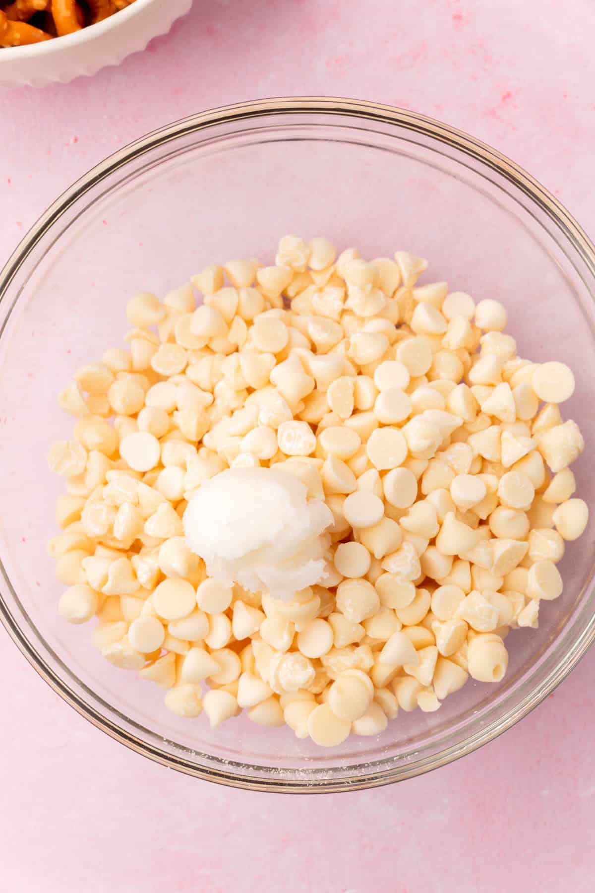 A glass bowl of white chocolate chips with coconut oil before melting.