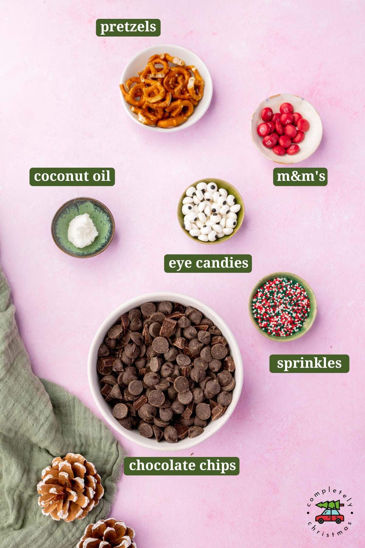 Small ingredients in bowls to make chocolate reindeer bark on a pink table with text overlays over each ingredient.