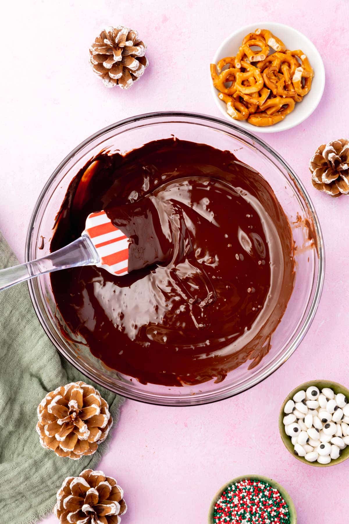 A glass mixing bowl with melted semi-sweet chocolate chips and a Christmas spatula.