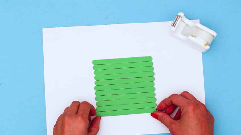 Hands placing green popsicle sticks next to each other in a row.