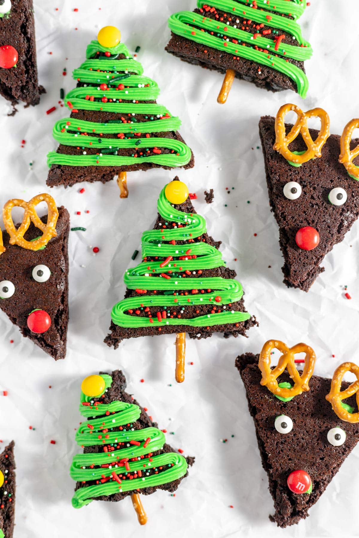 Christmas brownies in the shape of triangles and decorated like Christmas trees and reindeer with green frosting, candy eyes, M&Ms and pretzels.