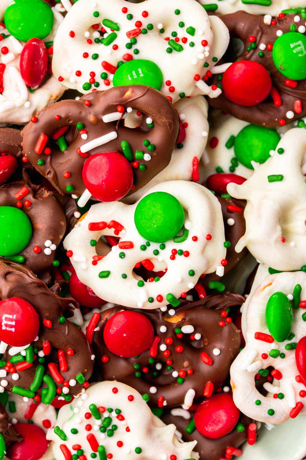 A closeup of white chocolate and semi-sweet chocolate covered Christmas pretzels topped with Christmas sprinkles and red and green M&Ms.