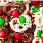 A closeup of white chocolate and semi-sweet chocolate covered Christmas pretzels topped with Christmas sprinkles and red and green M&Ms.