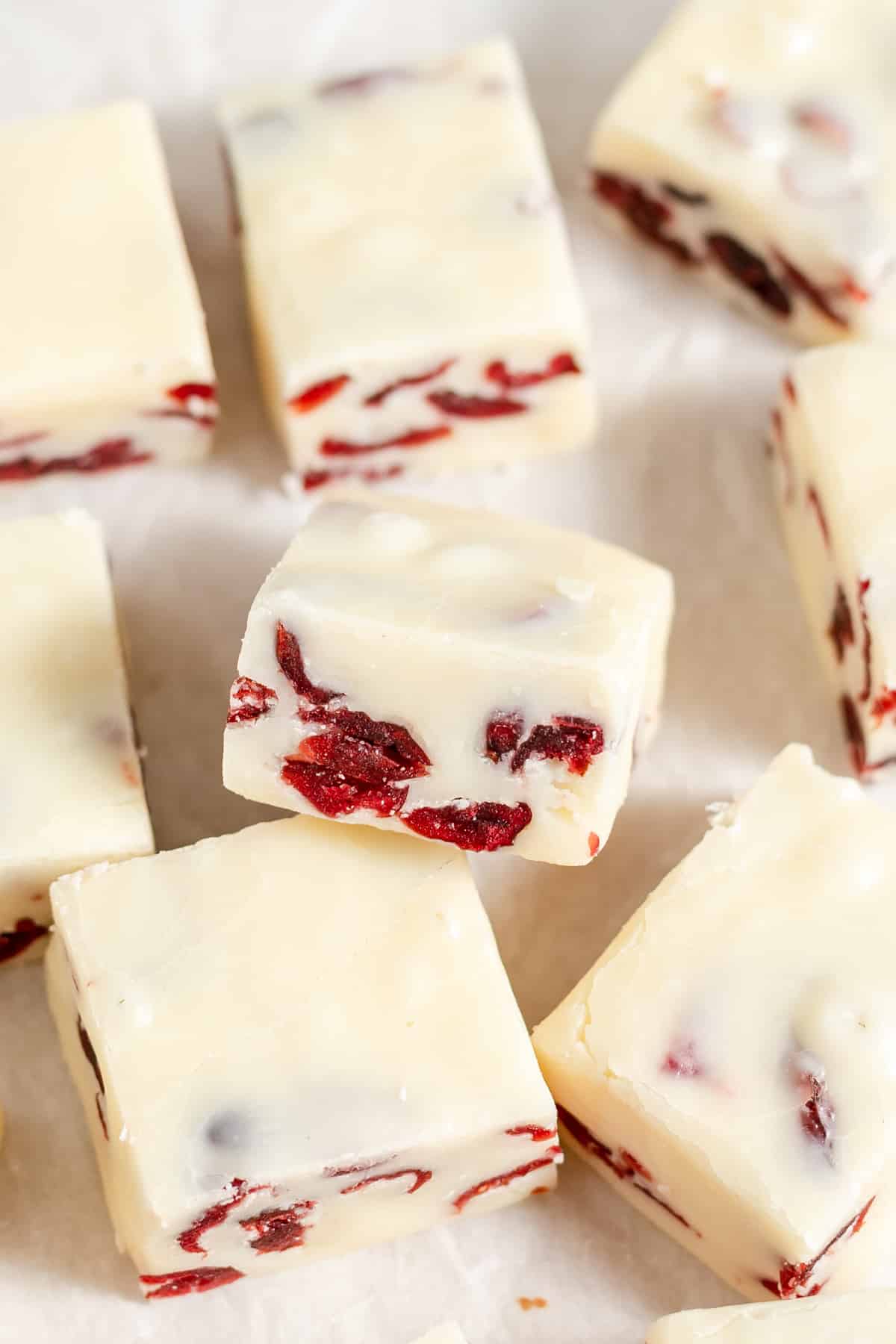 Squares of cranberry white chocolate fudge staggered on a piece of parchment paper.