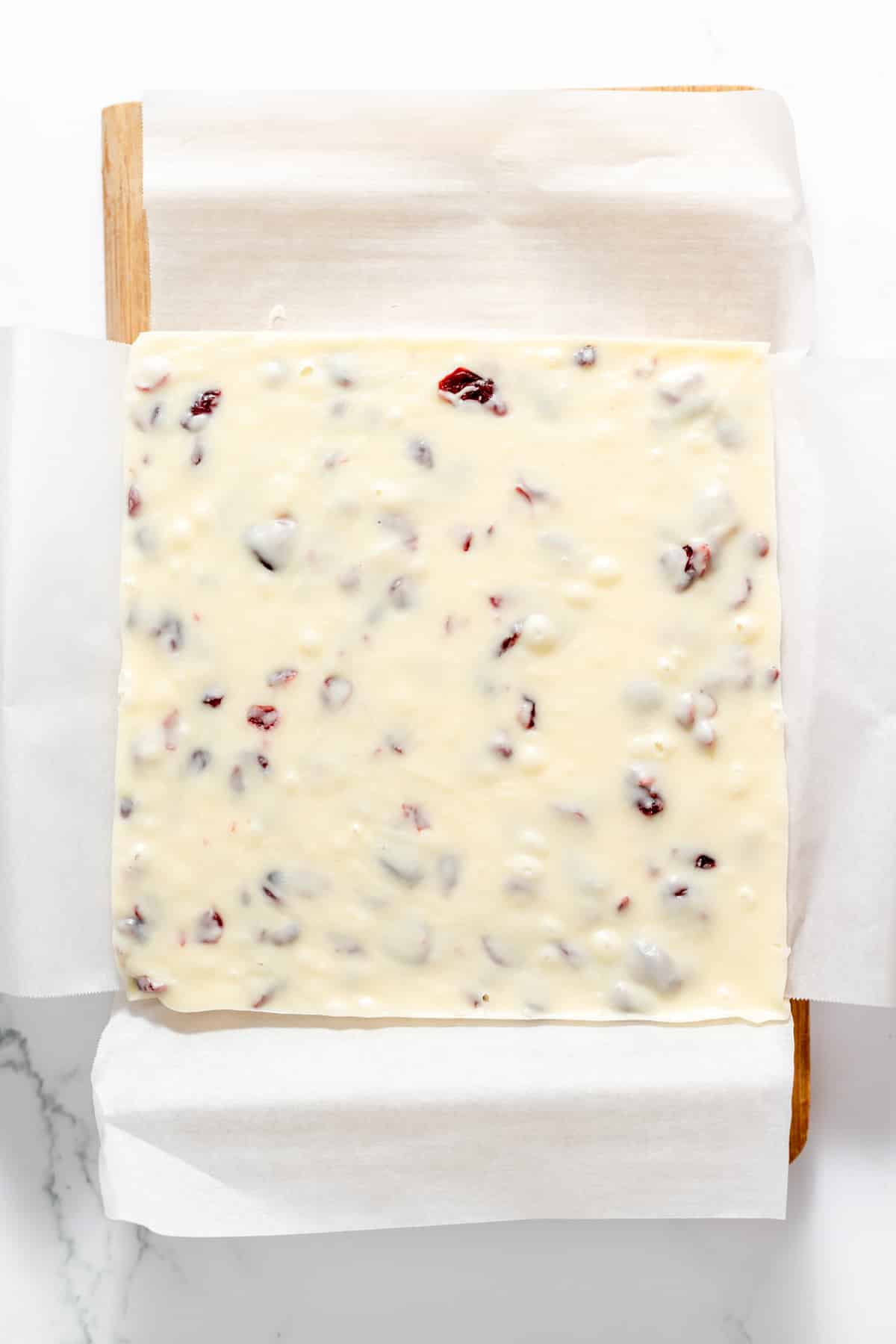 Cranberry white chocolate fudge on a cutting board lined with parchment paper before slicing into squares.