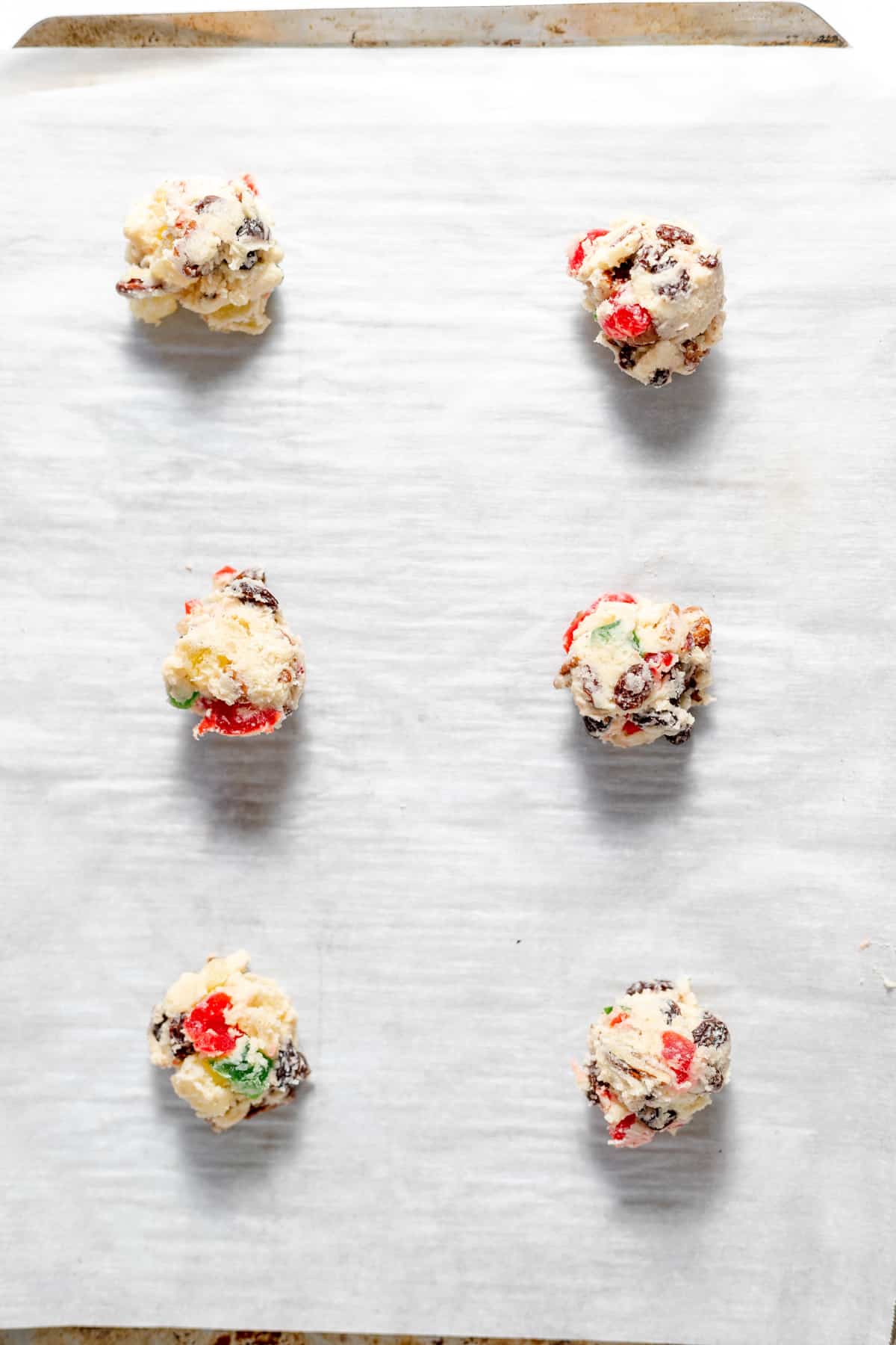 Six balls of fruitcake cookie dough on a parchment lined baking sheet before baking.