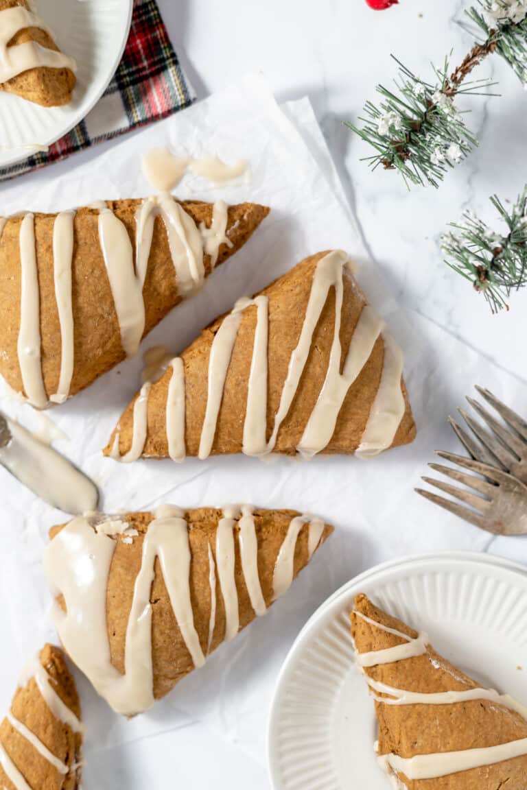 Gingerbread scones on a white table with forks, winter greenery, and a plaid napkin.