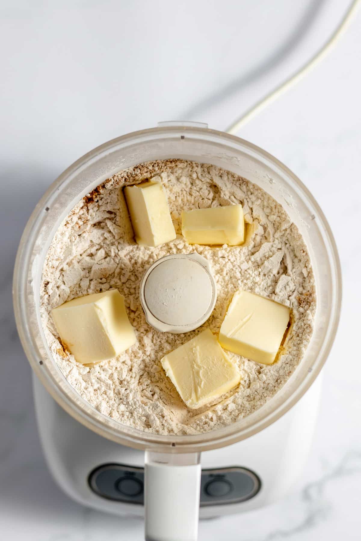 A food processor with dry ingredients and cubes of butter before mixing together.