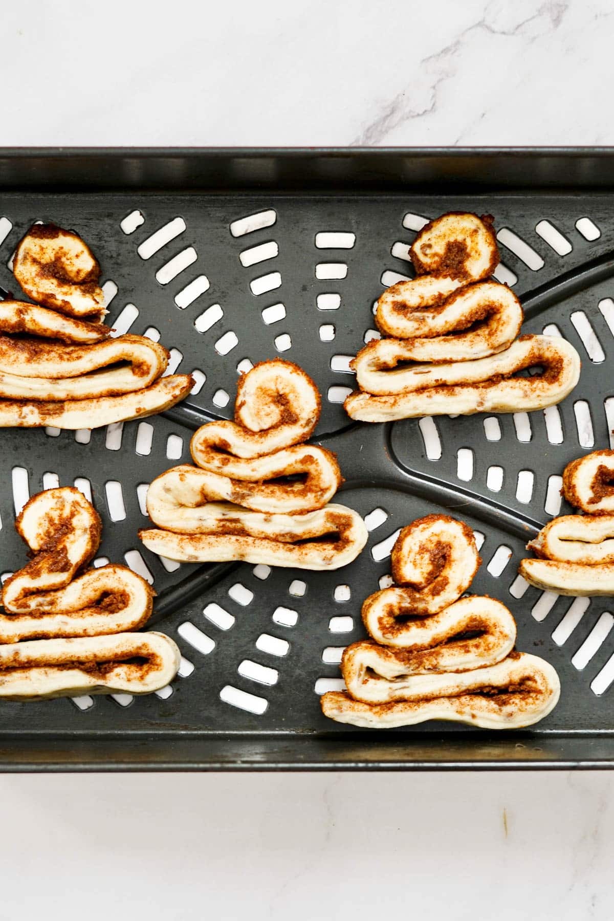 Unbaked cinnamon roll dough in the shape of Santa hats in an air fryer basket before cooking.