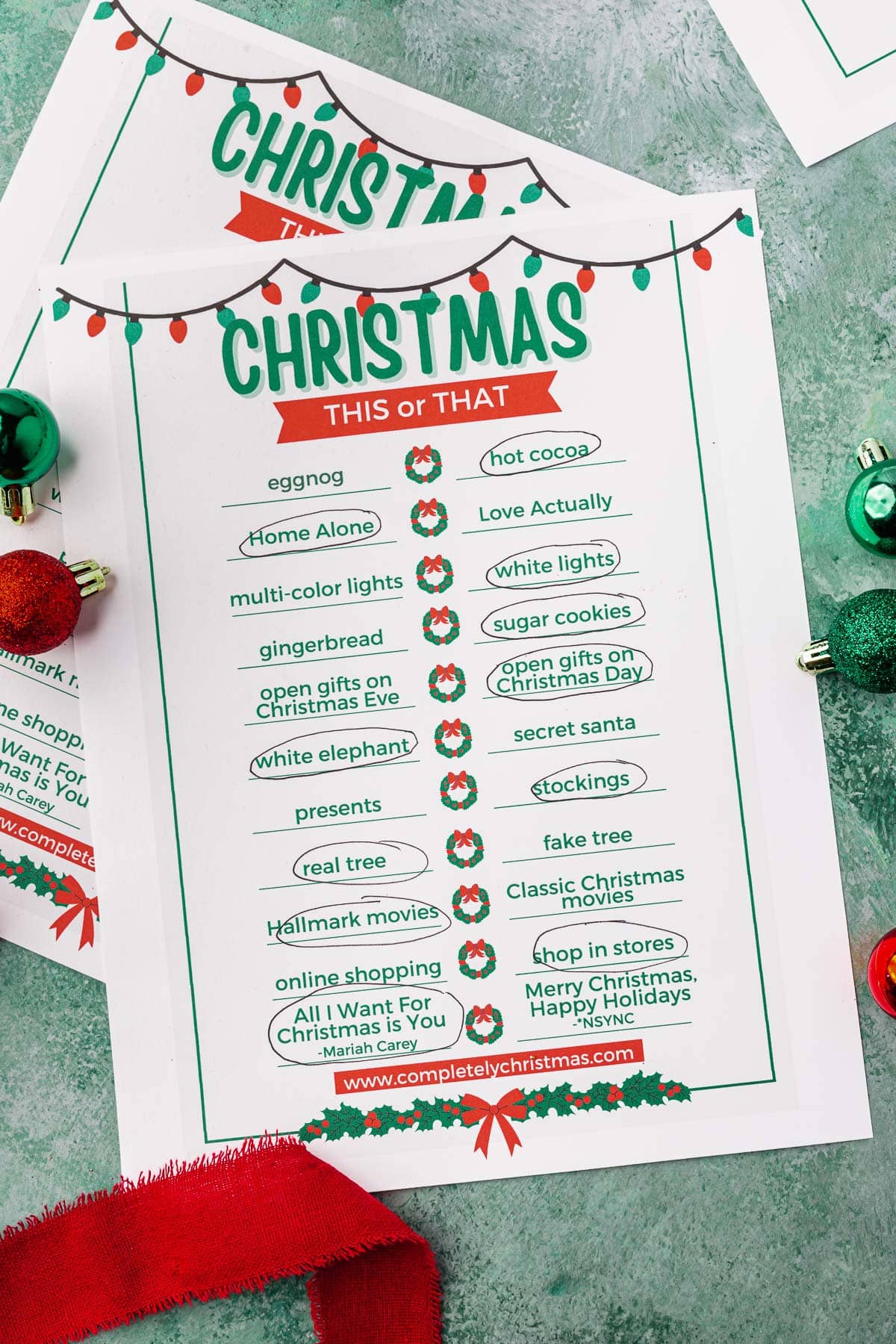 Pages of a Christmas This or That printable game on a green table.