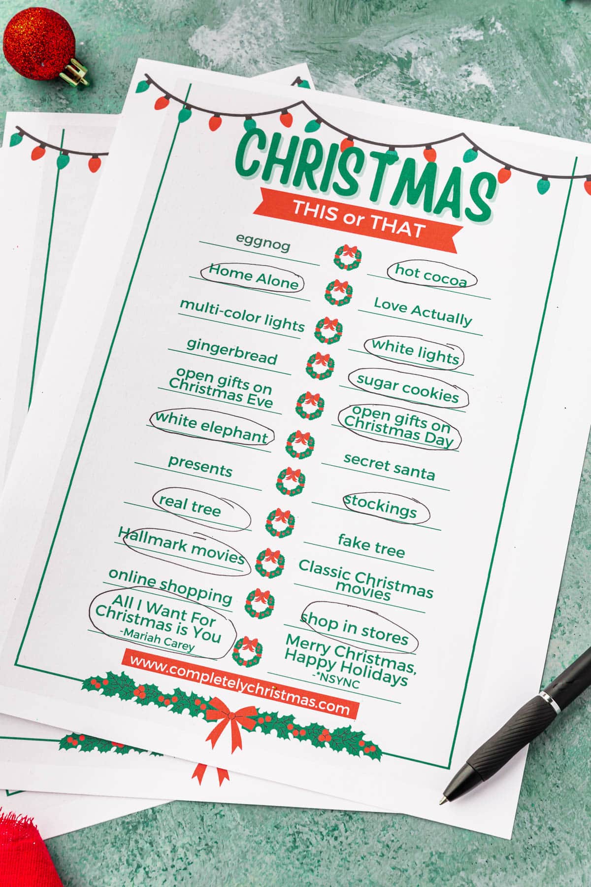 Pages of a Christmas This or That printable game on a green table.