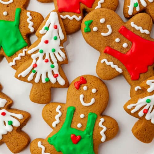 A close up of gingerbread cookies decorated with royal icing in red, green and white to look like Christmas trees and gingerbread men.