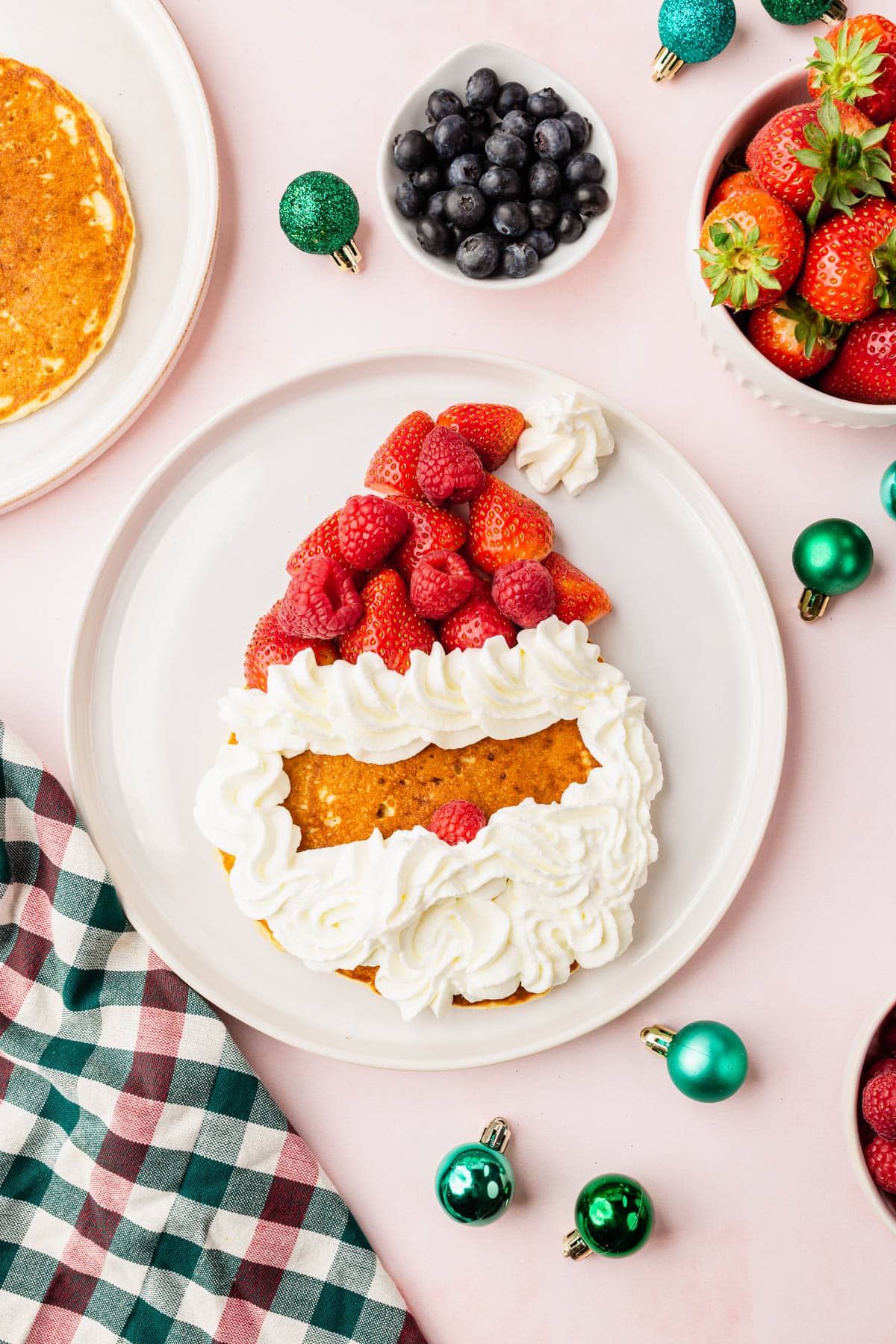 A santa pancake being decorated with raspberries, strawberries and whipped cream.