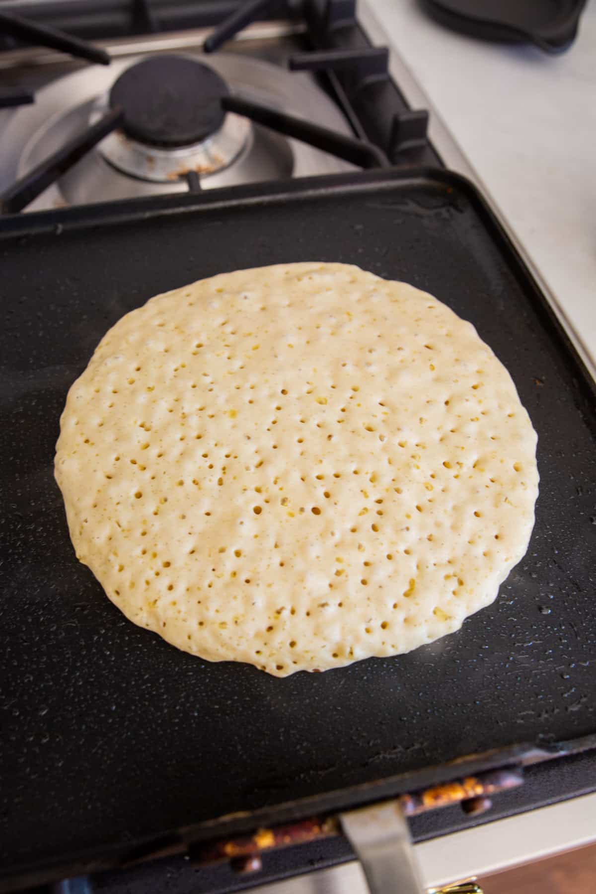 A pancake bubbling up on a square griddle on the stove top.