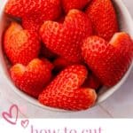 A bowl filled with heart shaped strawberry halves on a pink herringbone table.
