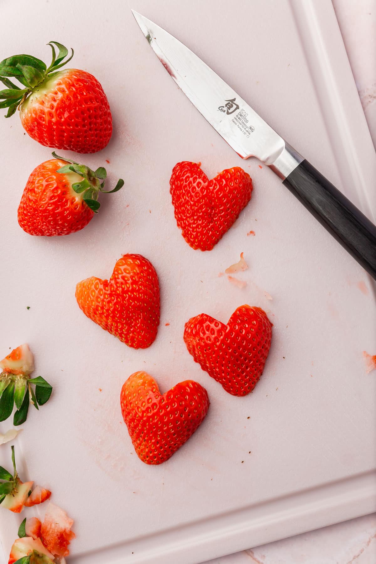 Strawberries sliced to look like hearts on a cutting board with a knife.