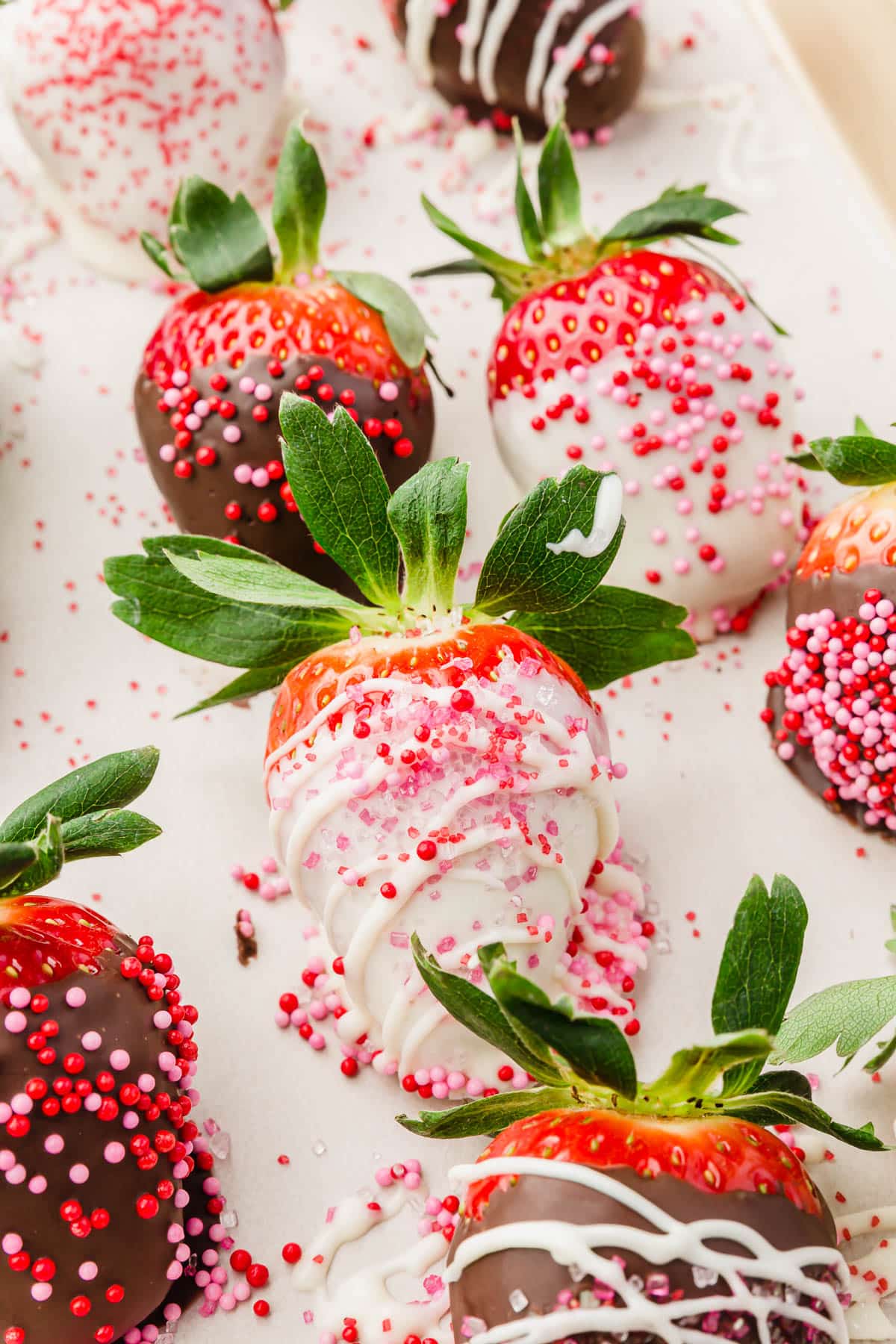 A baking sheet lined with parchment paper with strawberries that have been dipped in white chocolate or dark chocolate and decorated with pink and red sprinkles.