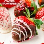 A closeup of a strawberry decorated in dark chocolate, a drizzle of white chocolate, and red and pink sprinkles for Valentine's Day with more strawberries behind it.