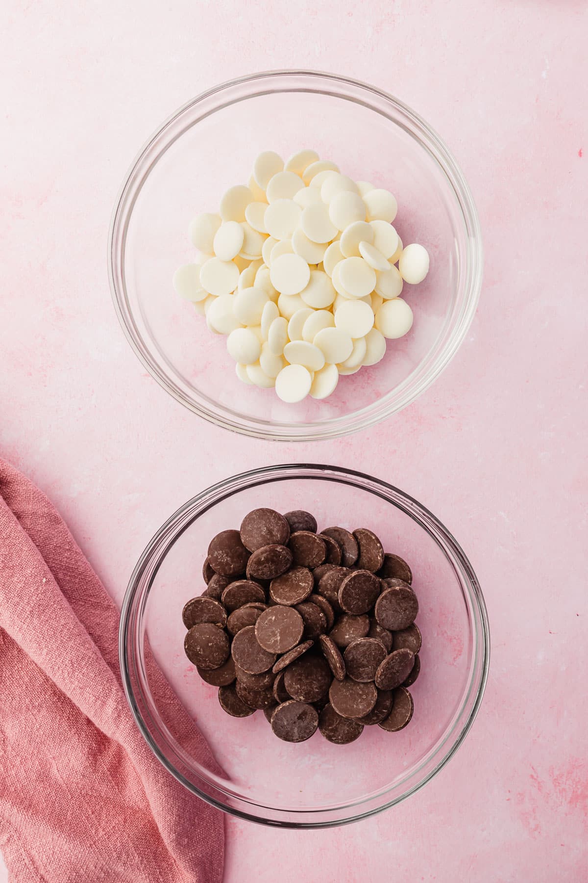 Two glass mixing bowls filled with white chocolate candy melts and dark chocolate candy melts before each bowl has been melted.