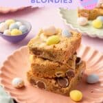 A stack of three Easter blondies with mini chocolate eggs on a pink scalloped plate.