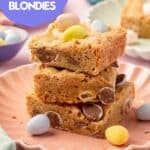 A stack of three Easter blondies on a pink plate topped with mini chocolate eggs.