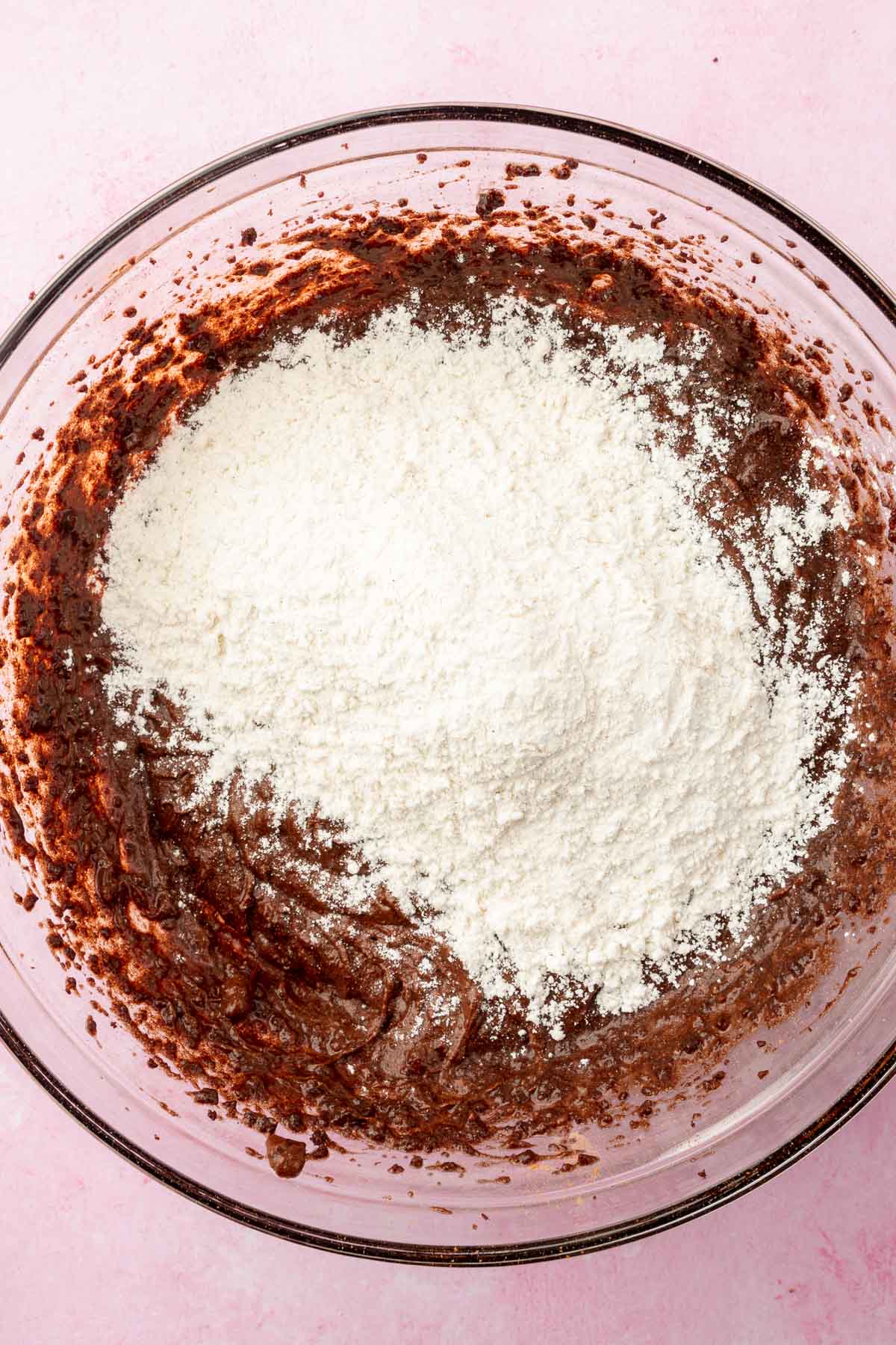 A glass mixing bowl with chocolate batter topped with all-purpose flour before mixing together.