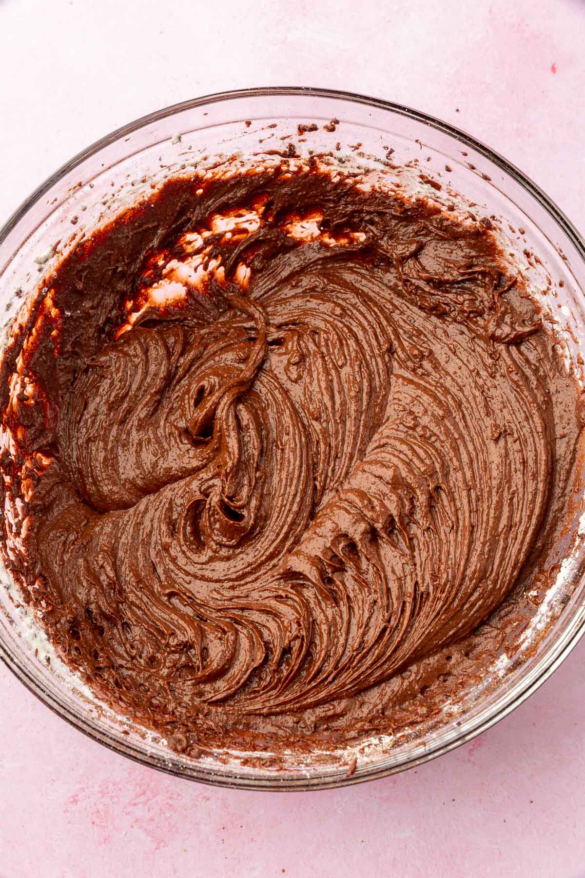 A glass mixing bowl with raw brownie batter in it.