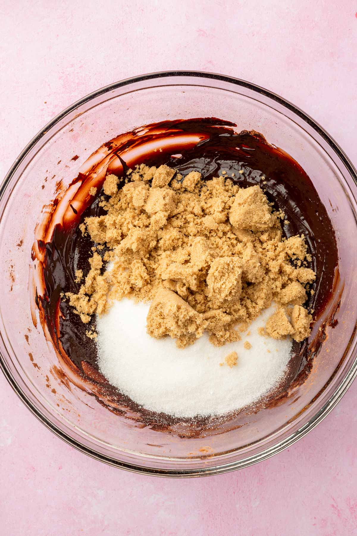 A glass mixing bowl with melted chocolate topped with brown sugar and granulated sugar.