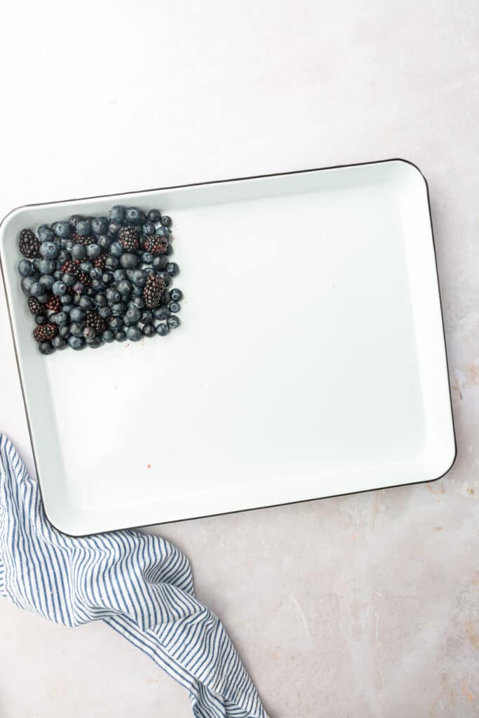 Blueberries and blackberries in a square shape in the upper left hand corner of a white baking sheet to make an American flag charcuterie board.