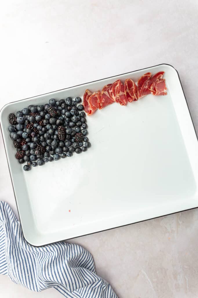 Blueberries, blackberries and capoccolo being assembled to make an American flag charcuterie board.