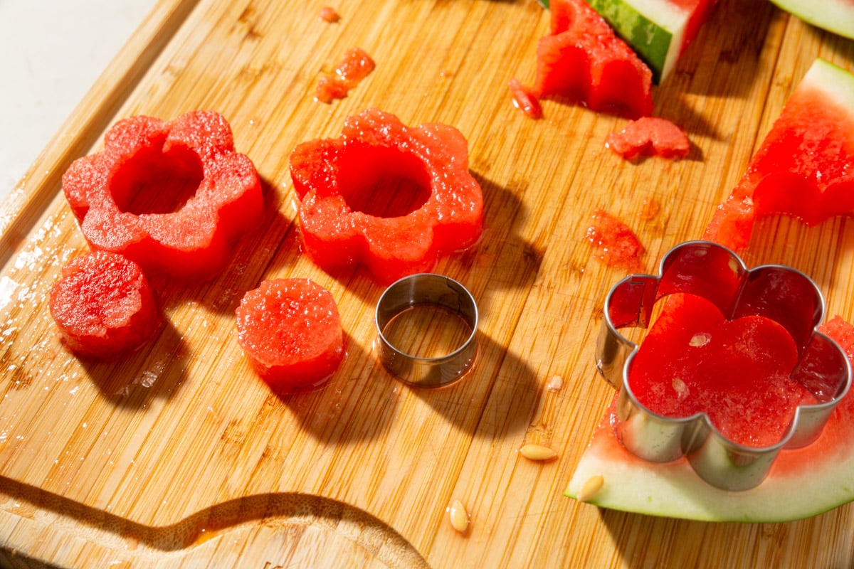 Metal cookie cutters and watermelon flower cutouts with round centers on a wooden board.