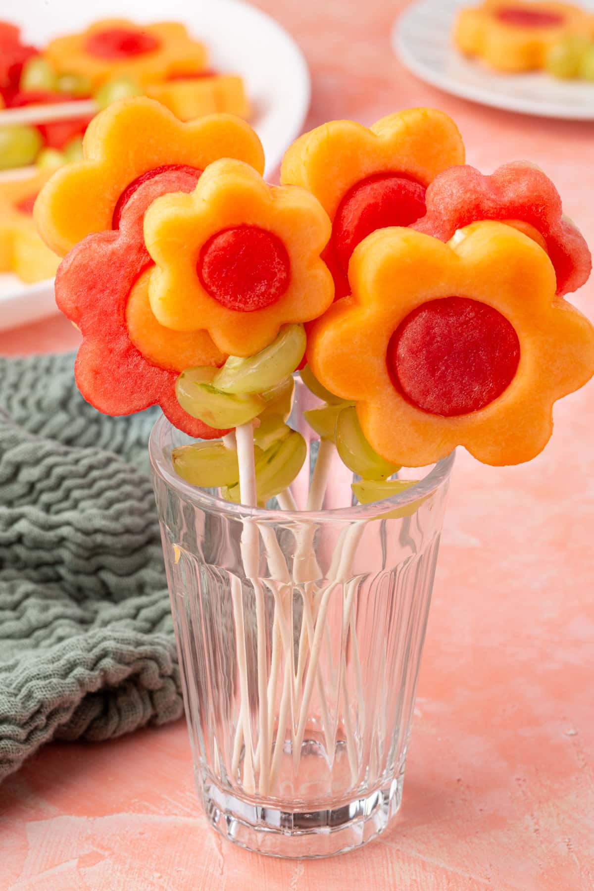 Flower fruit kabobs made with cantaloupe and watermelon in a clear glass, with green grapes as leaves.
