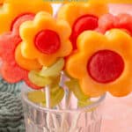 Colorful fruit kabobs with flower-shaped fruit and grape “leaves” displayed upright in a glass.