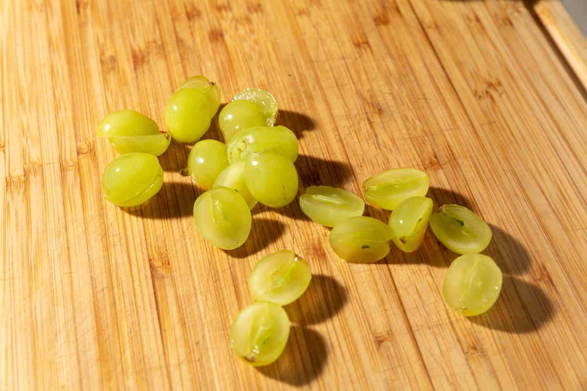 Halved green grapes scattered on a wooden cutting board, ready for kabob assembly.