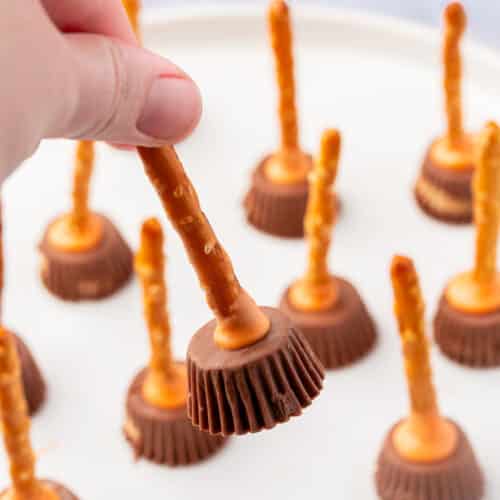 Close-up of a hand holding one peanut butter cup pretzel witch broom.