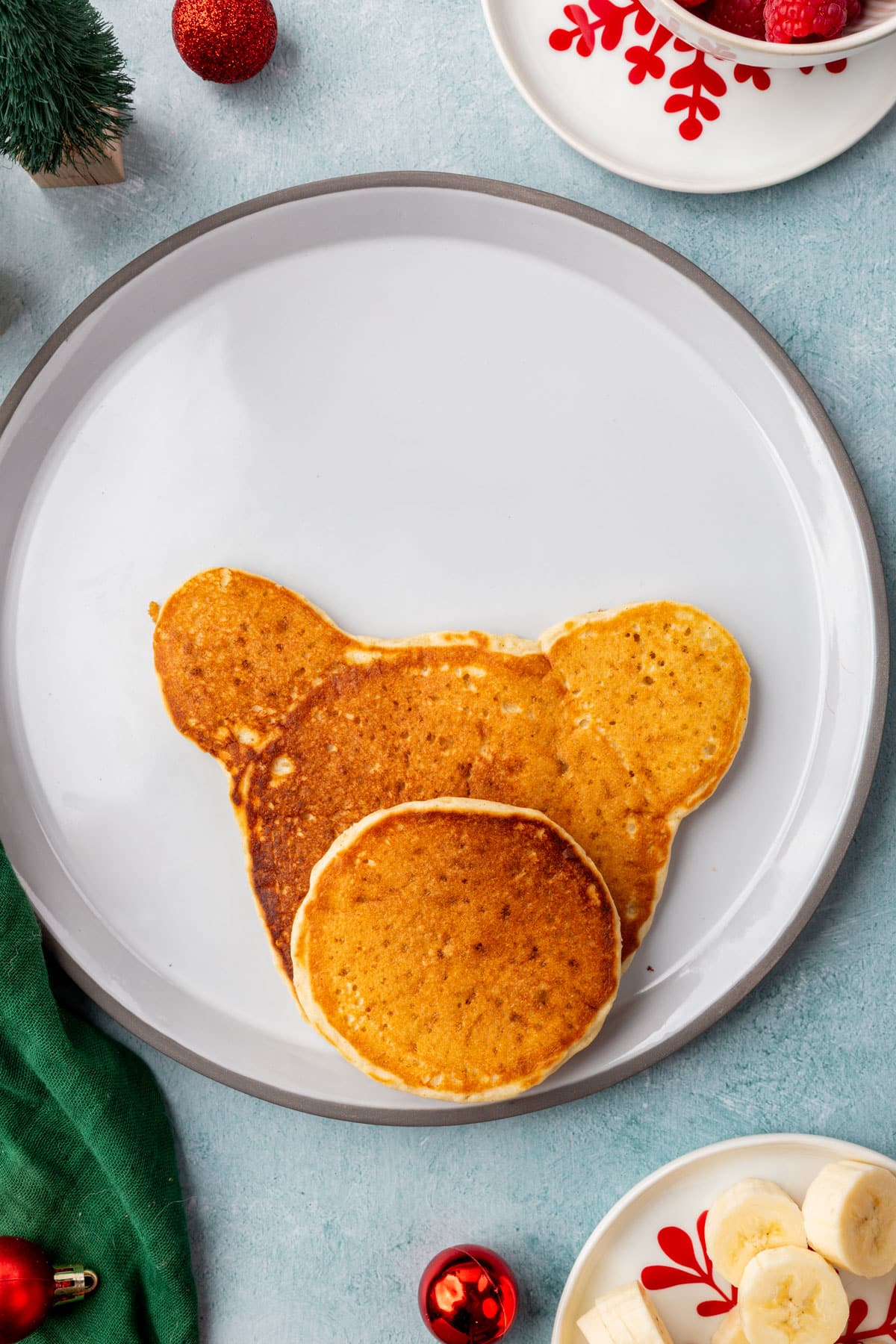 Two pancakes arranged on a plate to form the reindeer face shape, with one smaller pancake overlapping for the snout.