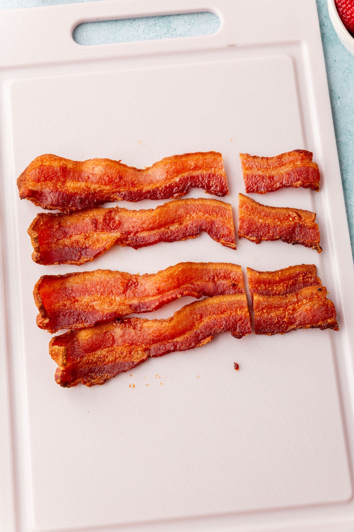 Four strips of cooked crispy bacon on a cutting board, ready to be used as antlers for reindeer pancakes.