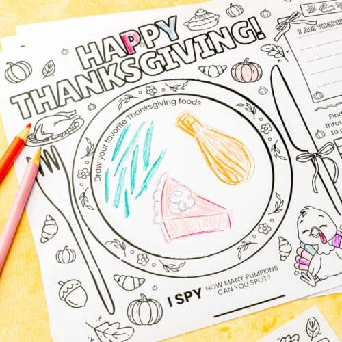 Close-up of Thanksgiving placemat with "Draw your favorite Thanksgiving foods" plate section partially colored in with green beans, corn, and pink pie slice, colored pencils visible on side.