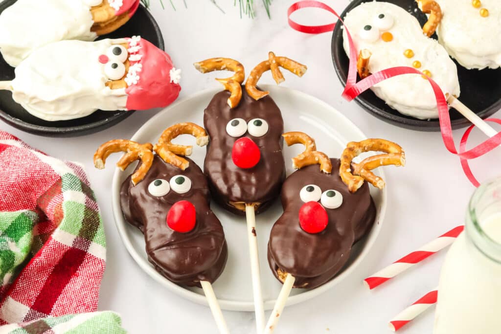 Three Nutter Butter Reindeer cookie pops on a plate with Santa and snowman cookies on either side.