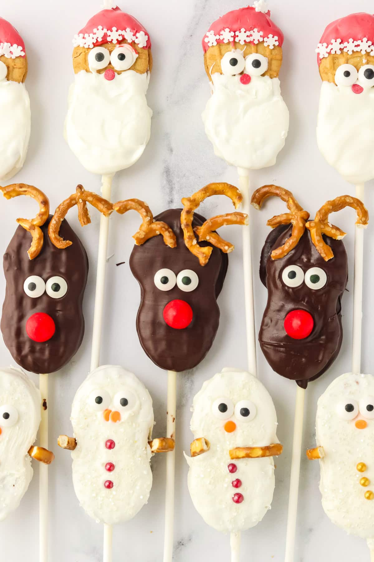 Rows of Nutter Butter Christmas cookie pops with Santas on top, Reindeer in the middle, and Snowmen on the bottom.