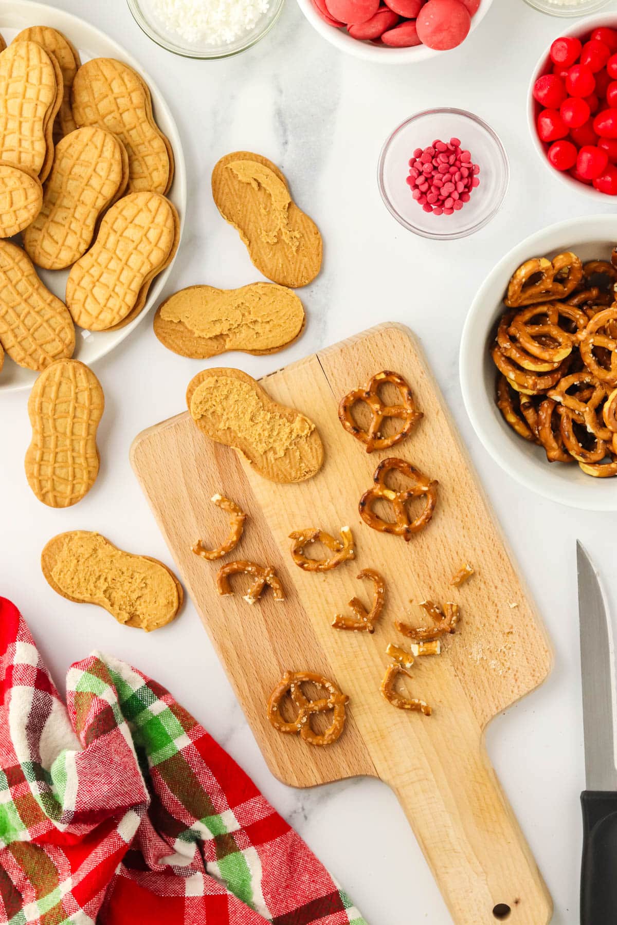 Pretzel twists being broken into pieces on a cutting board for reindeer antlers with Nutter Butter cookies nearby.