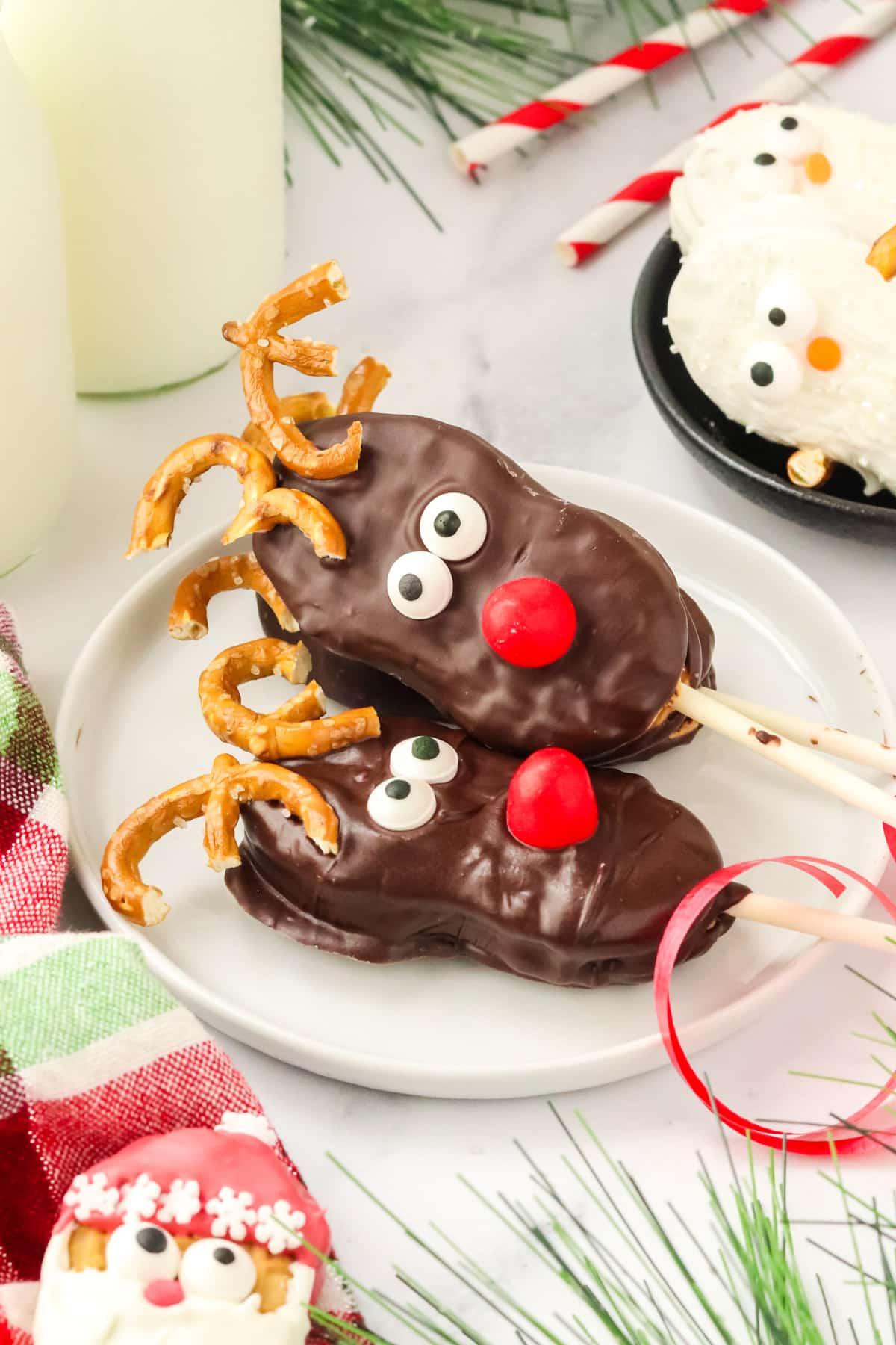 Two Nutter Butter Reindeer cookie pops stacked on a white plate with pretzel antlers and red candy noses.