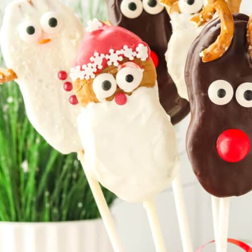 A group of Nutter Butter Christmas cookie pops with Santa, reindeer, and snowman designs in a festive display with greenery and red ribbon.