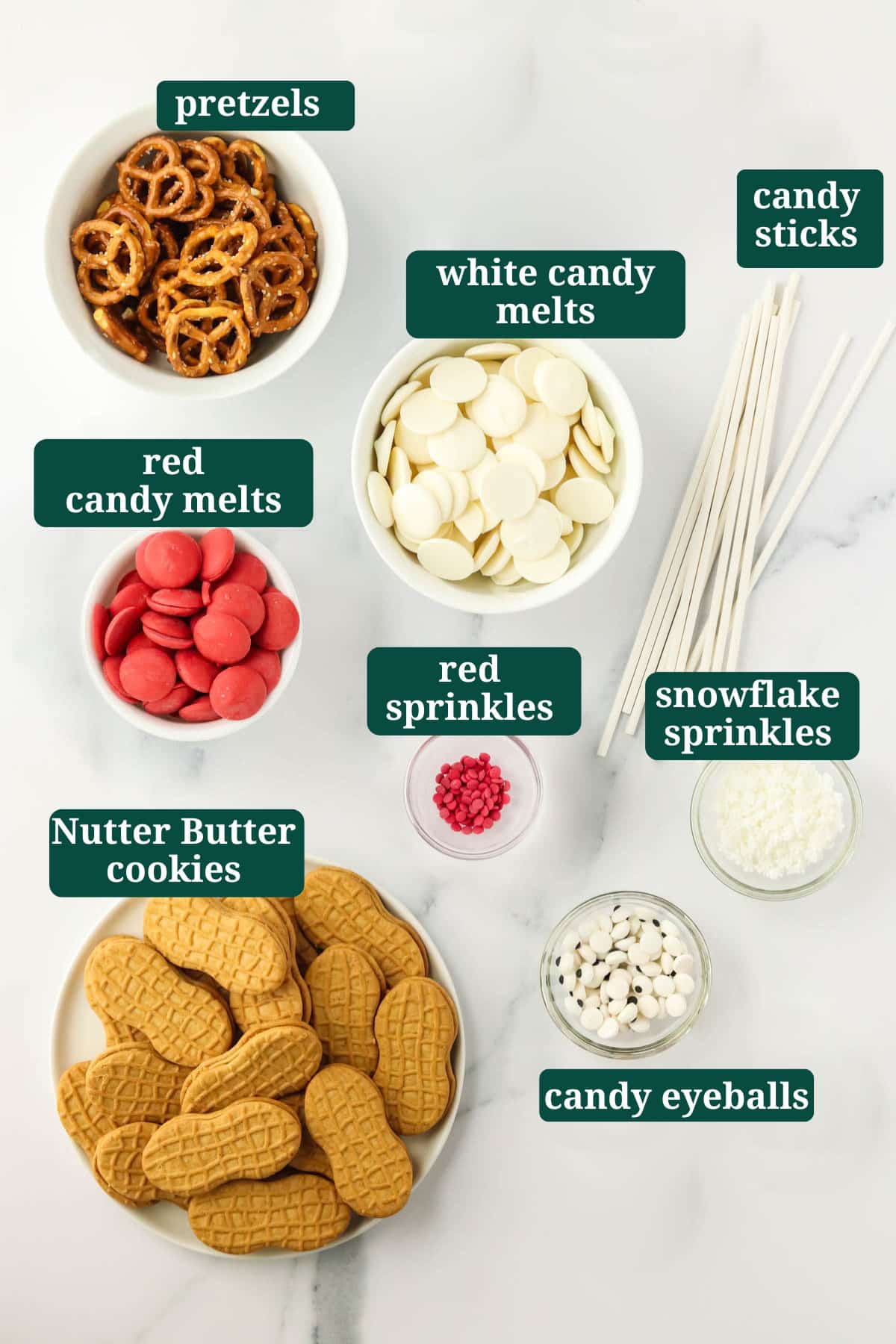 Ingredients for Nutter Butter Santa cookies including Nutter Butters, white and red candy melts, candy eyeballs, sprinkles, and candy sticks.