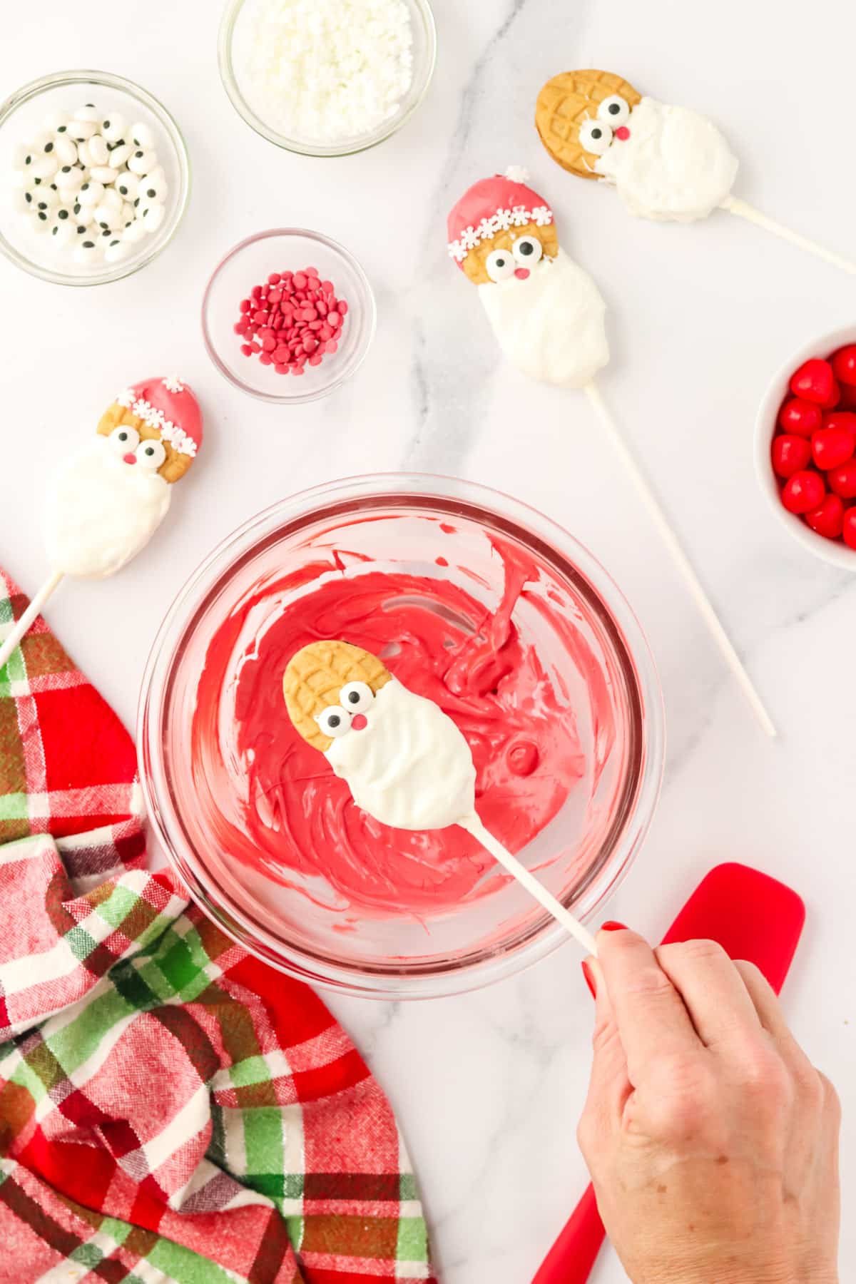 A hand dipping a Nutter Butter Santa cookie into red melted candy to create Santa's hat.