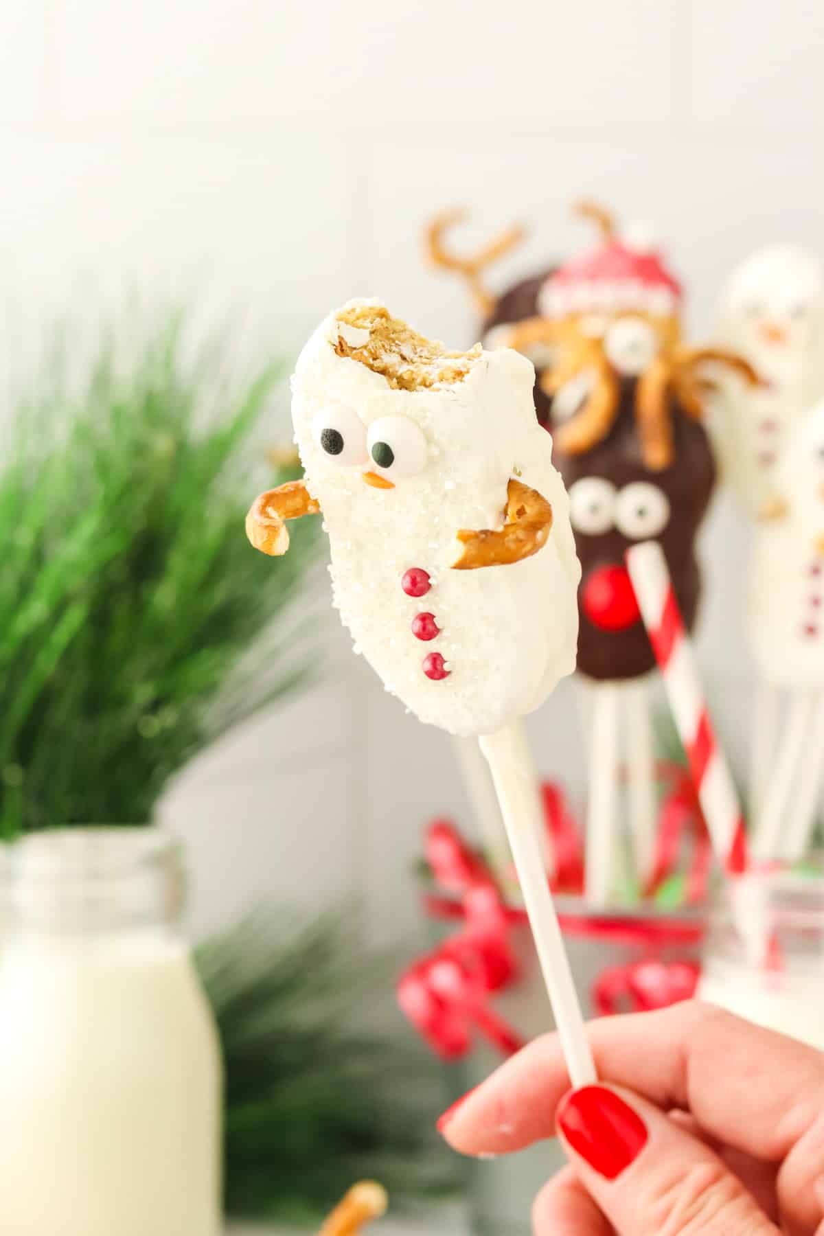 A hand holding a Nutter Butter Snowman cookie pop with a bite taken out showing the peanut butter cookie inside.